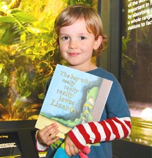 Boy holding 'The Boy who really, really, really, loves Lizards' book at the Vivarium at Manchester Museum