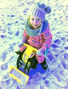 Girl on a rid-on digger playing in the snow