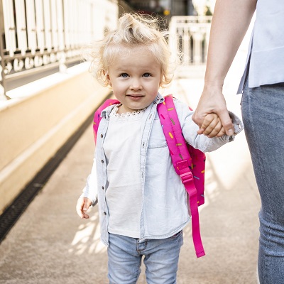 Cute child with backpack holding mother's hand outdoors