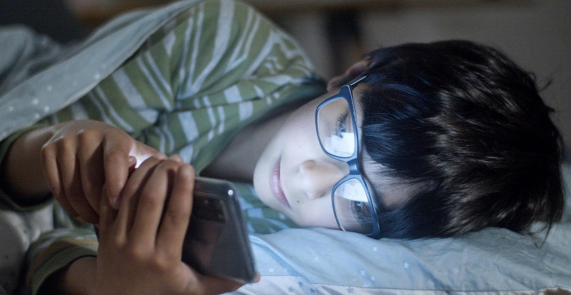 Boy is in bed and on the phone 